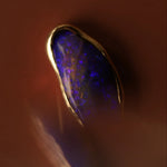 Close-up of a gold necklace with a blue opal stone on a dark background
