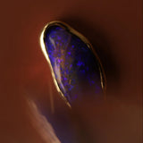 Close-up of a gold necklace with a blue opal stone on a dark background