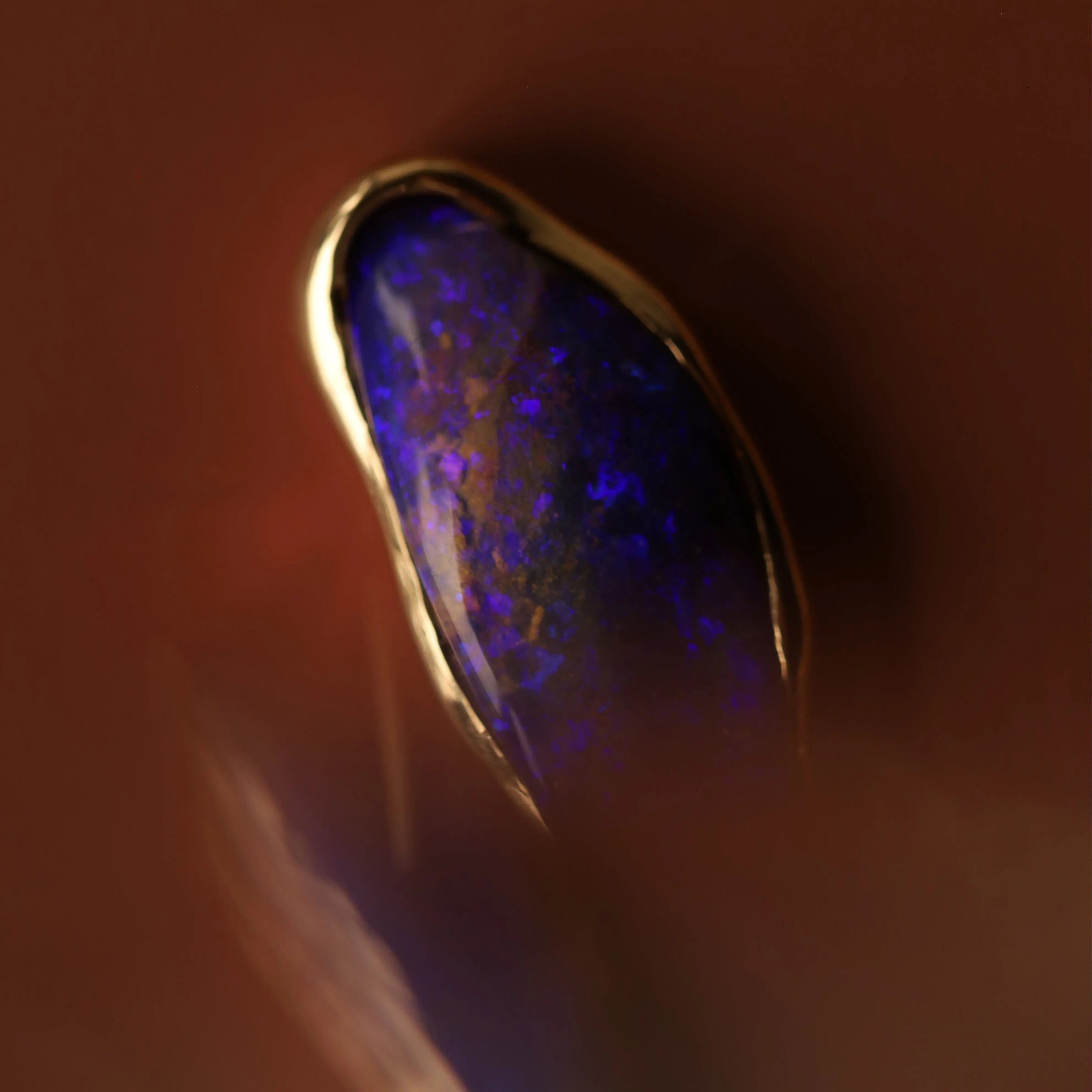 Close-up of a gold necklace with a blue opal stone on a dark background