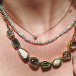 Close-up of a person wearing a layered necklace with gemstones on a light skin background