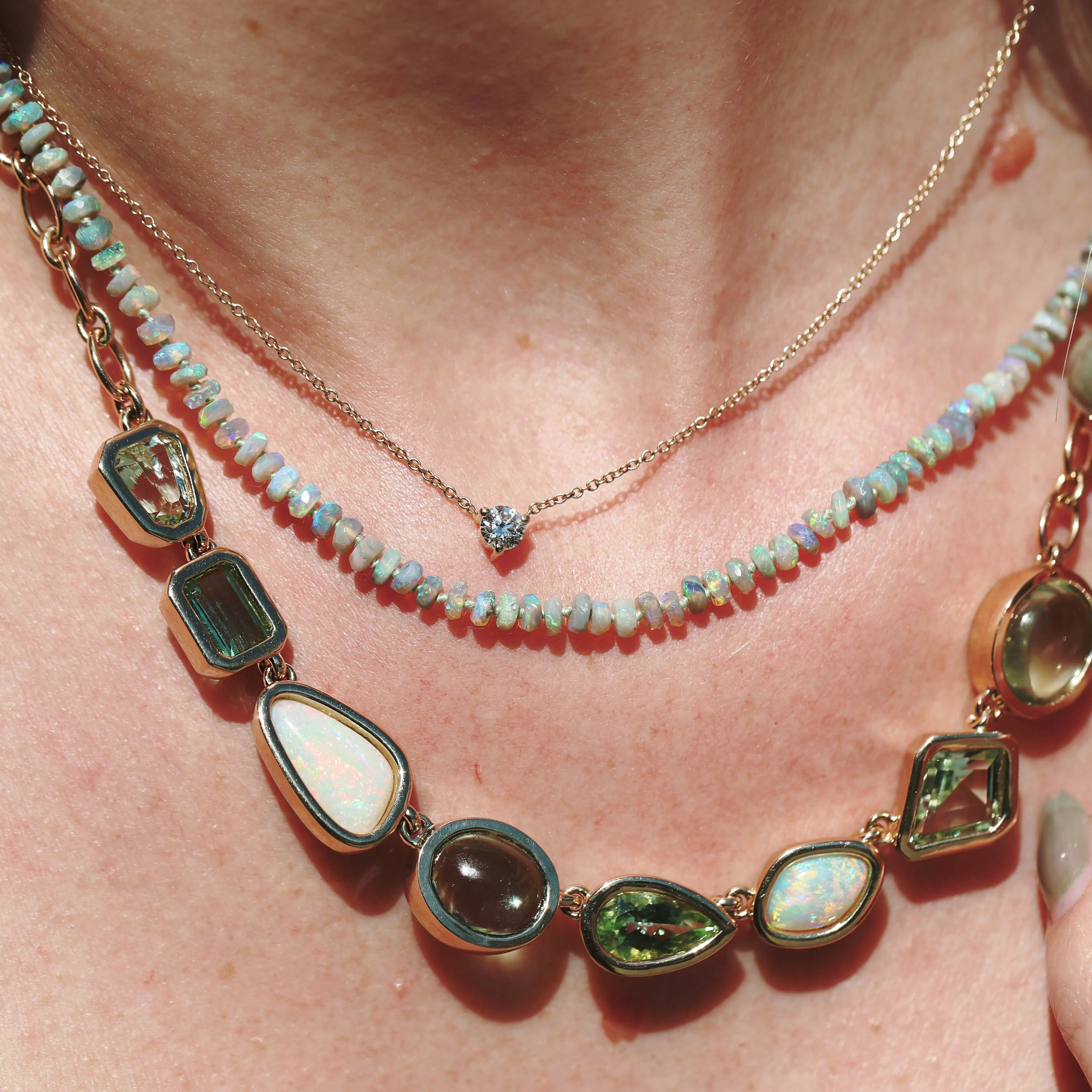 Close-up of a person wearing a layered necklace with gemstones on a light skin background