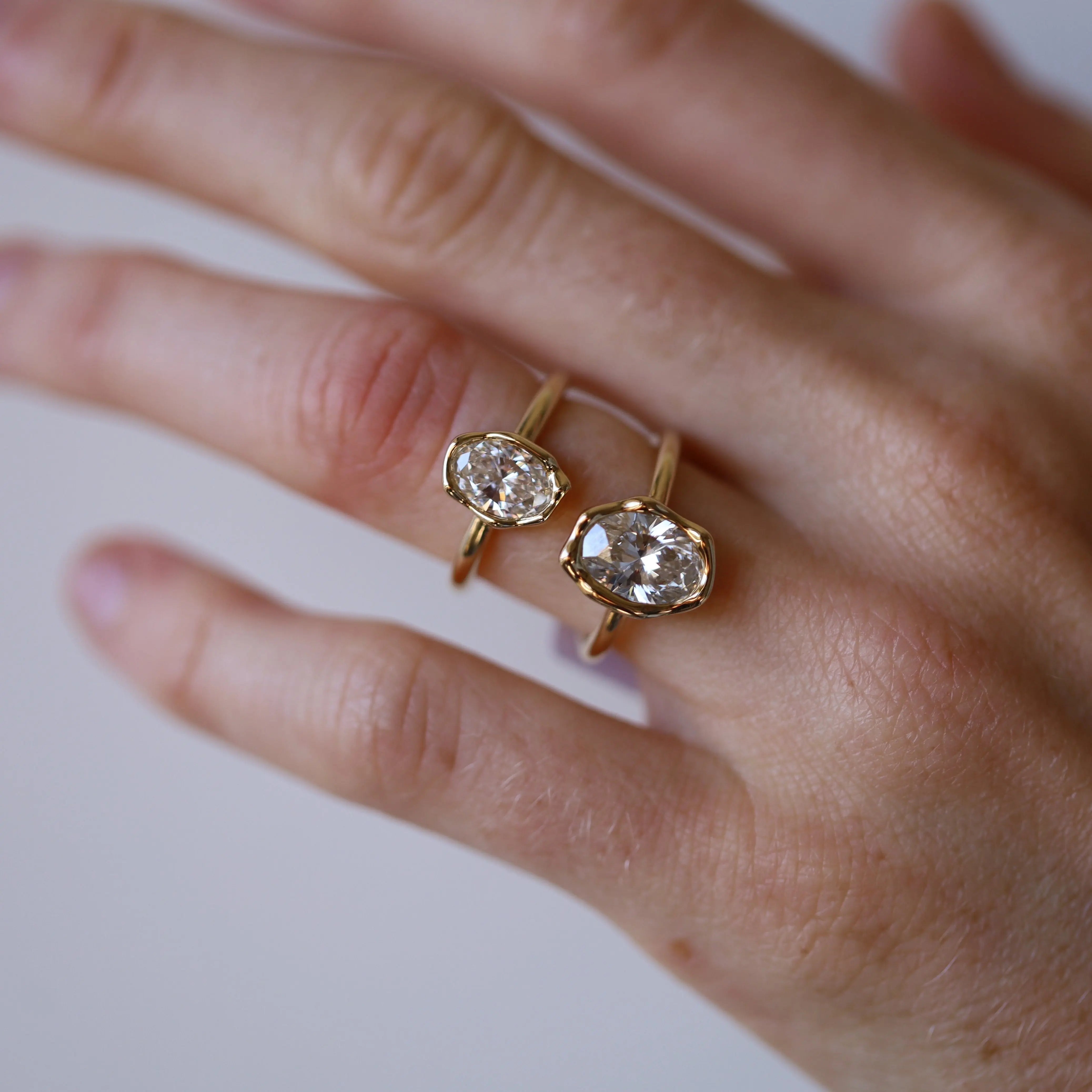 Hand wearing two gold rings with clear gemstones on a light background