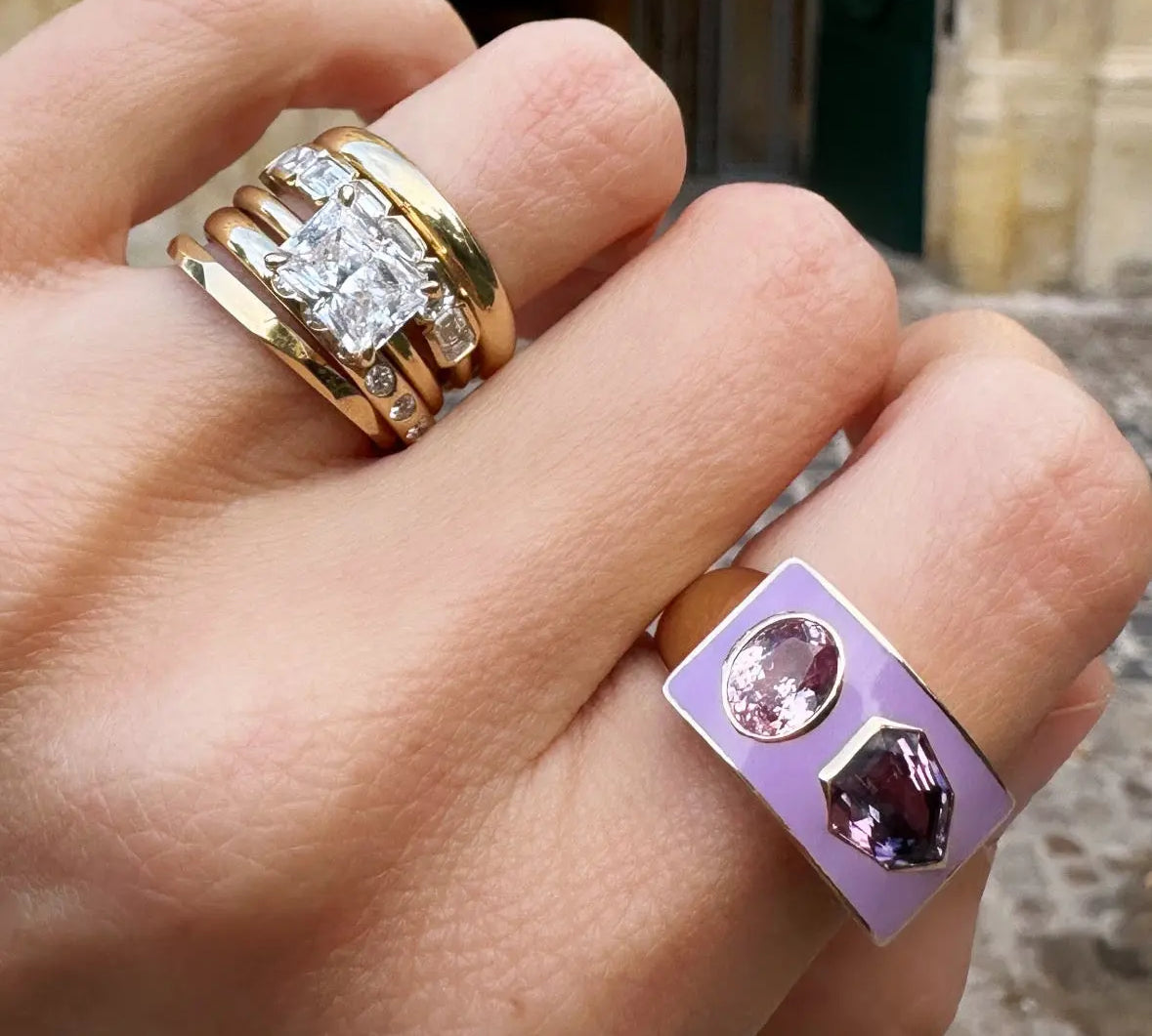 Hand wearing two rings with a blurred background of a building entrance.