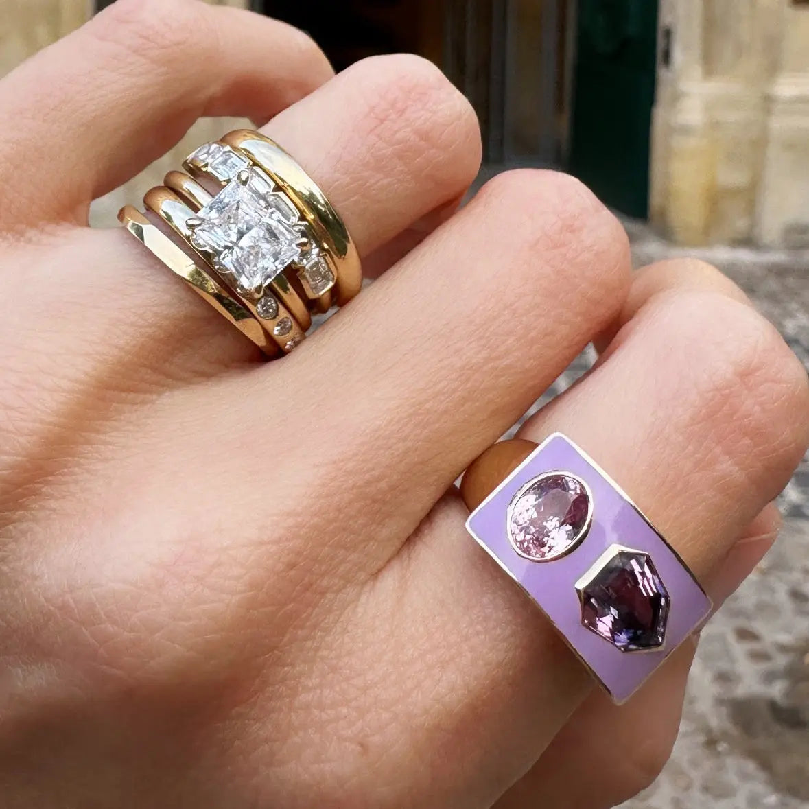 Hand wearing two rings with a blurred background of a building entrance.