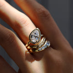 Gold ring with a diamond on a person's finger against a neutral background