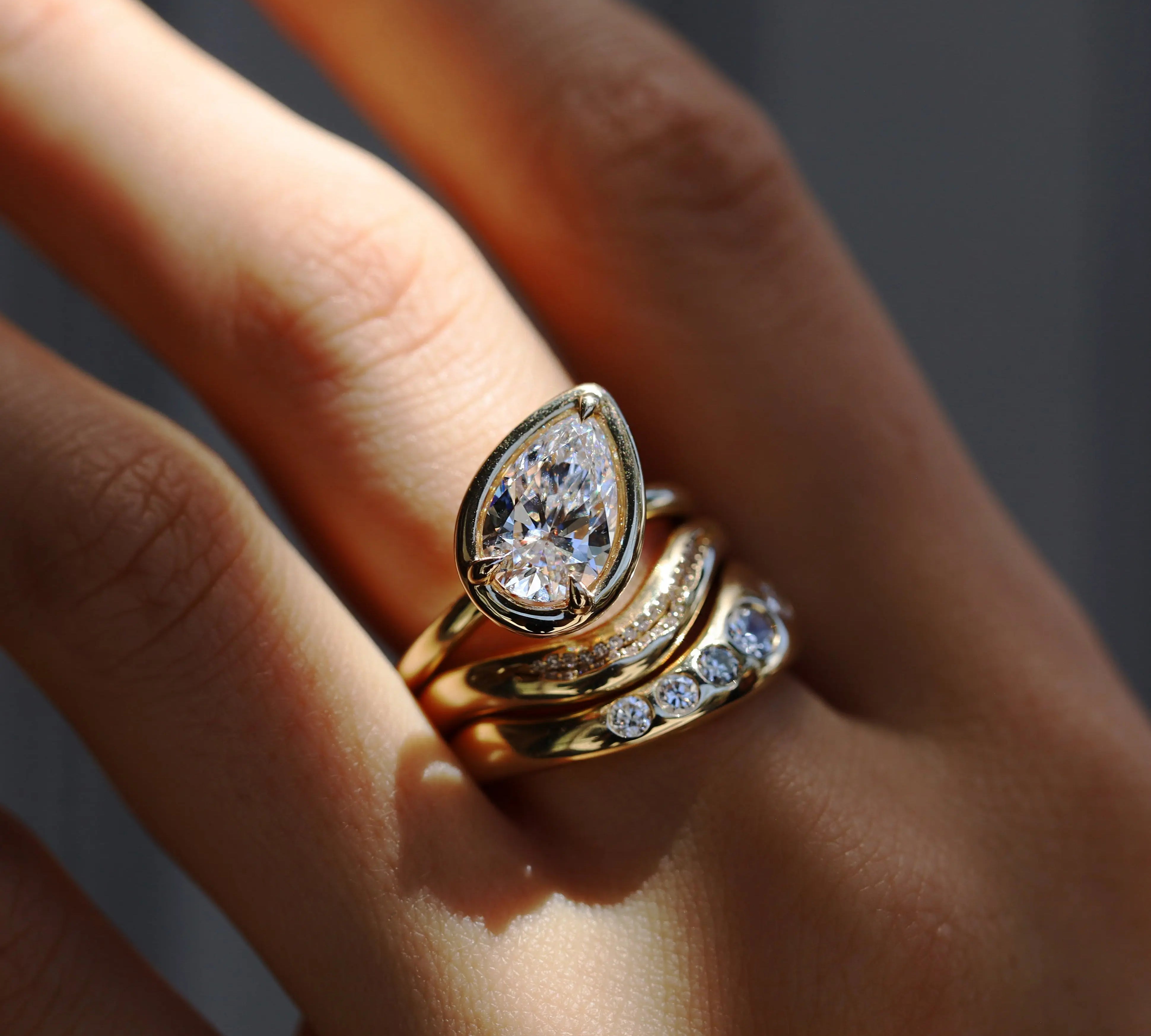 Gold ring with a diamond on a person's finger against a neutral background