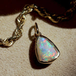 Opal pendant on a gold chain against a beige background