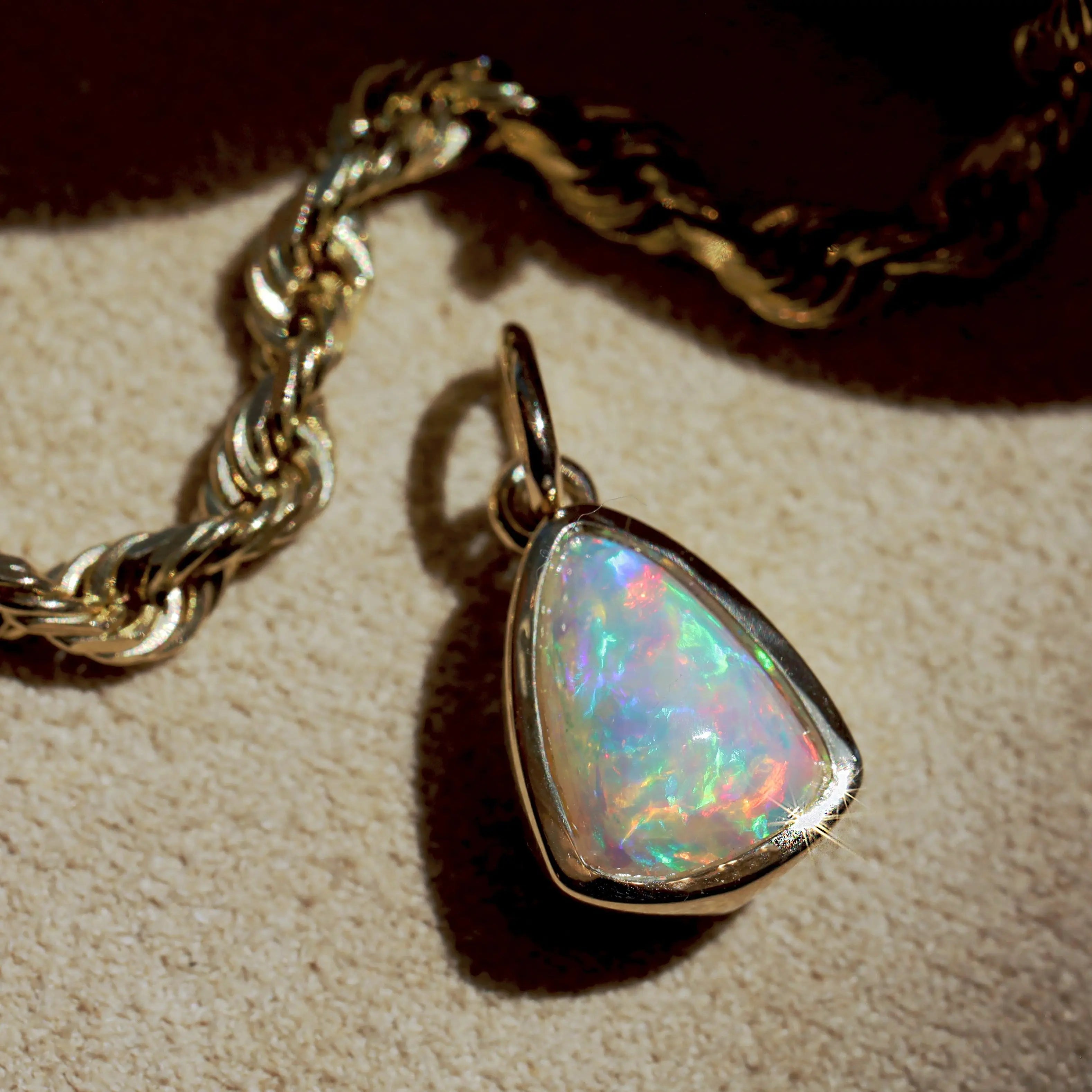 Opal pendant on a gold chain against a beige background