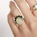 Close-up of a hand wearing an opal ring with gemstones on a light background