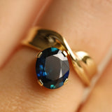 Close up image of gold ring with a blue gemstone on a person's finger