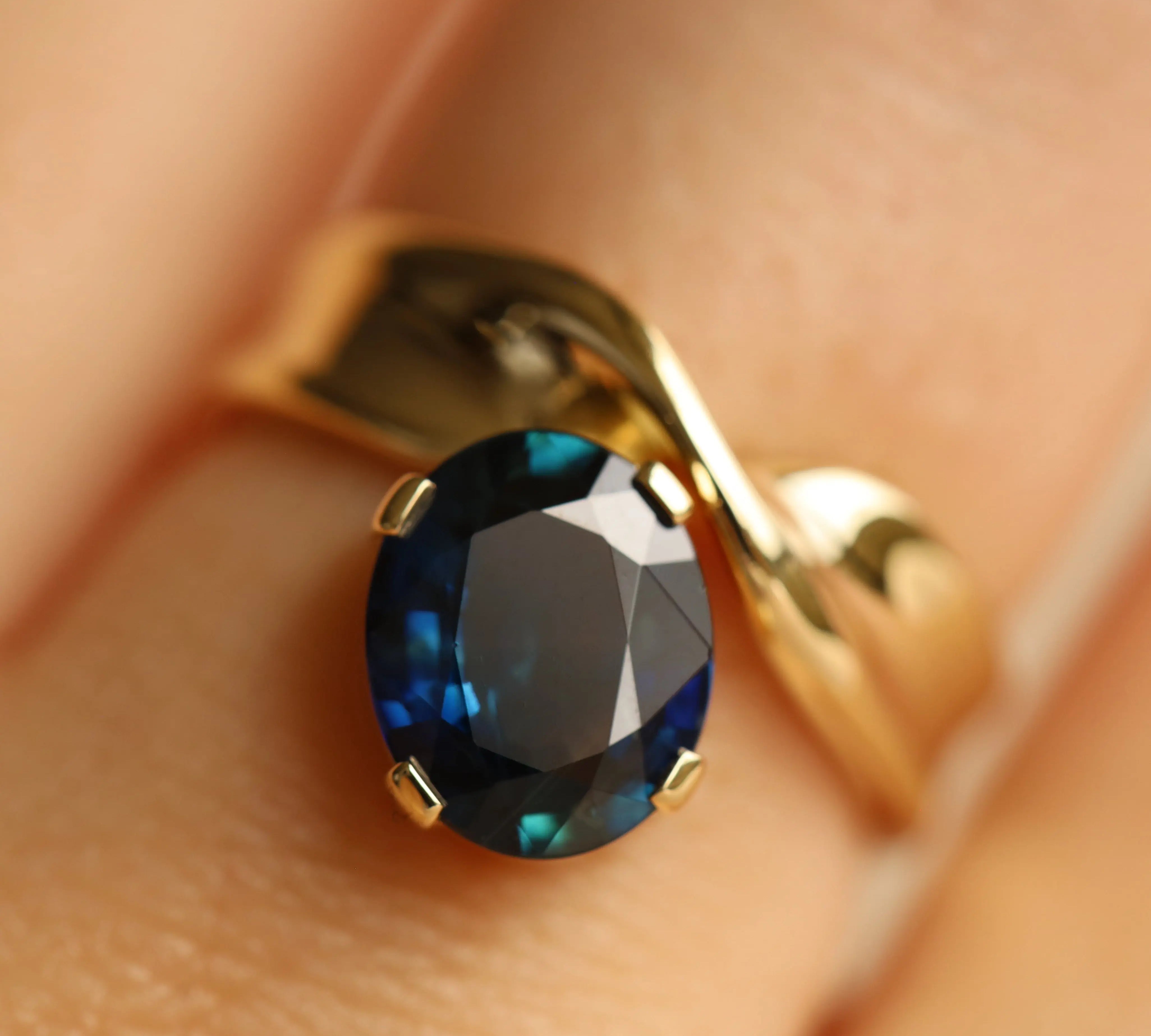 Close up image of gold ring with a blue gemstone on a person's finger