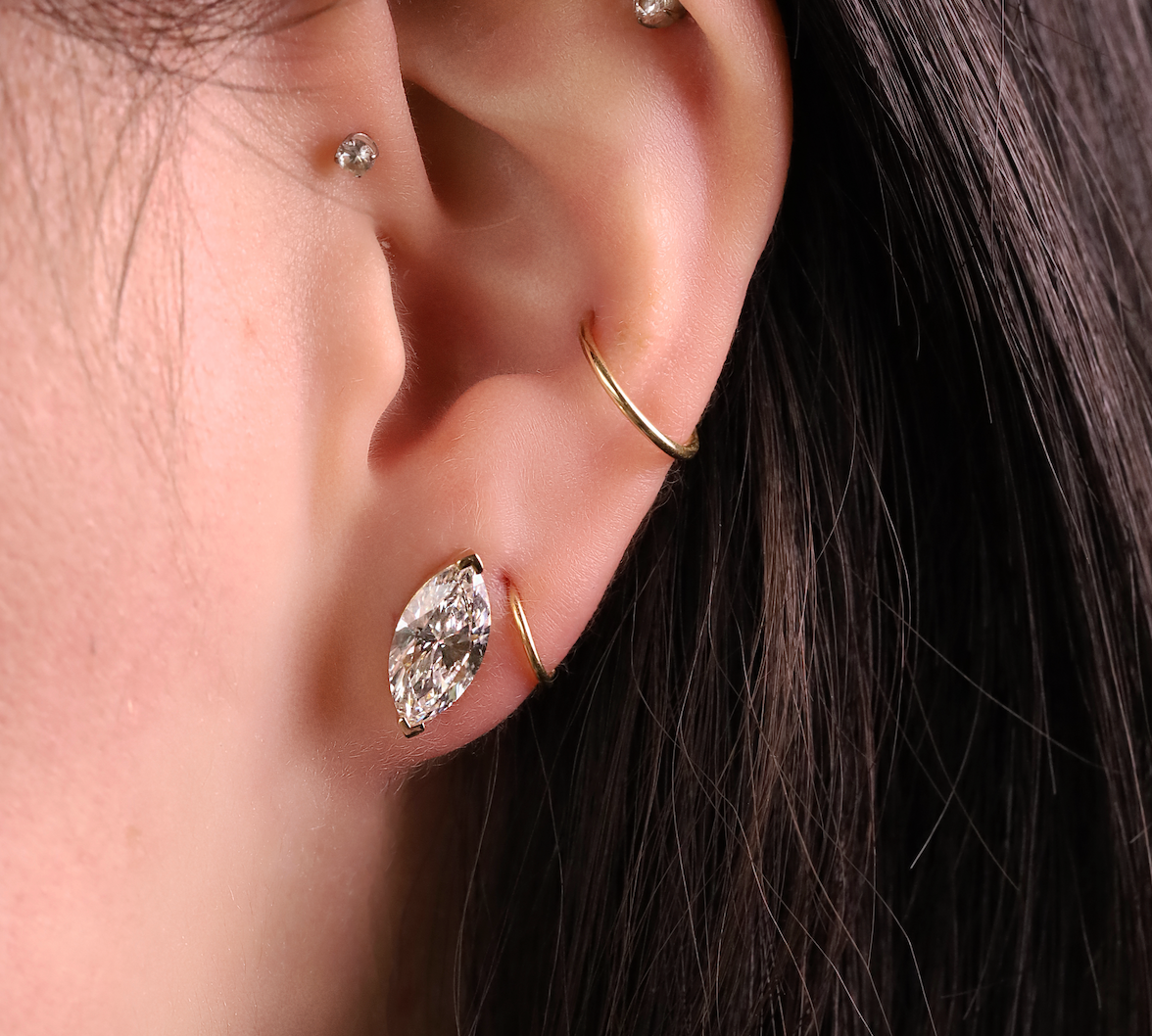 Close-up of an ear with diamond earrings and a gold ring.