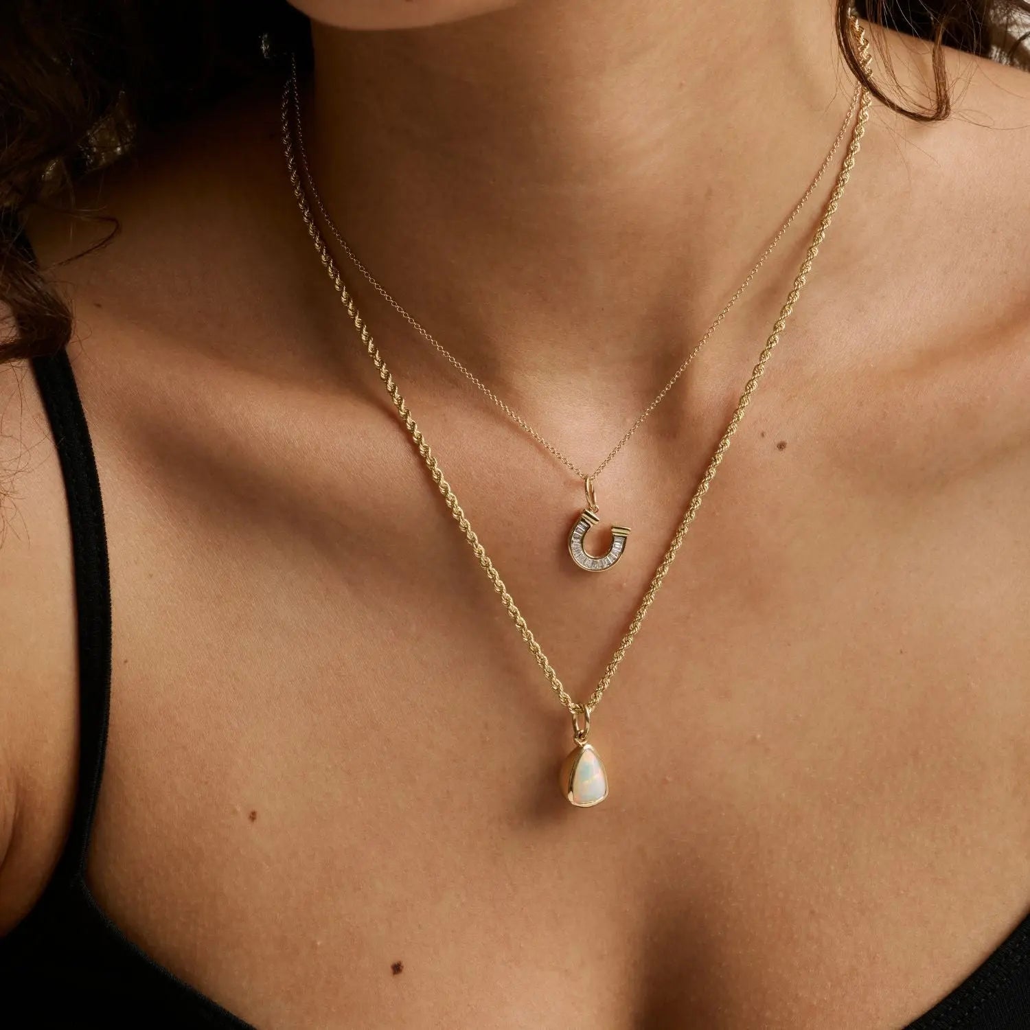 close up of woman's décolletage spotlighting two yellow gold chains of varying weights layered with charms