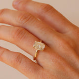 Gold ring with a diamond on a hand against a beige background