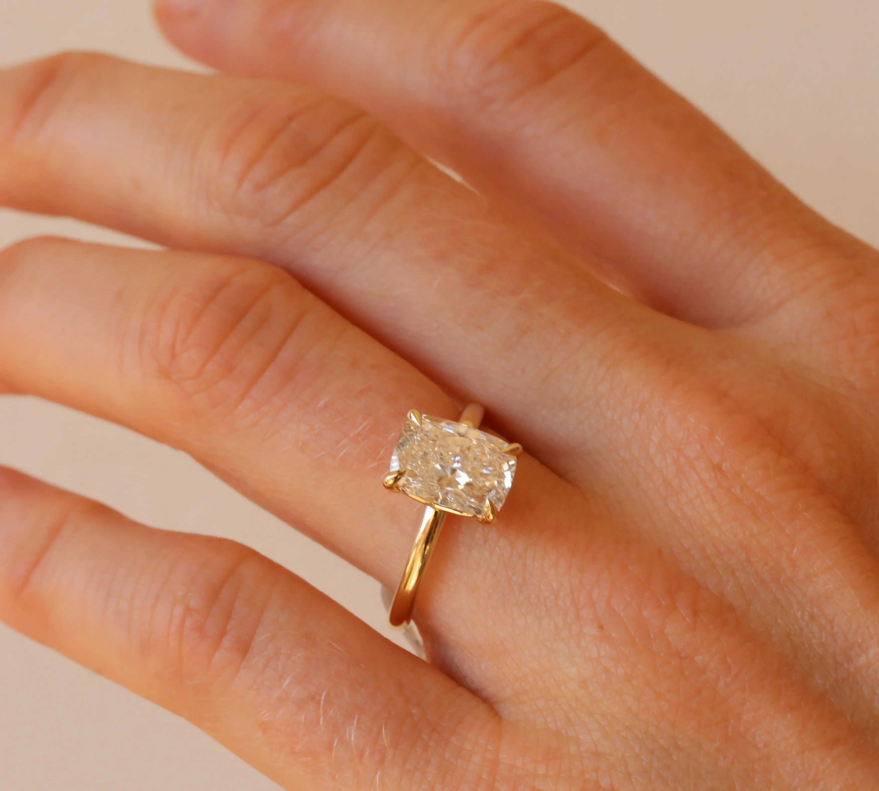 Gold ring with a diamond on a hand against a beige background