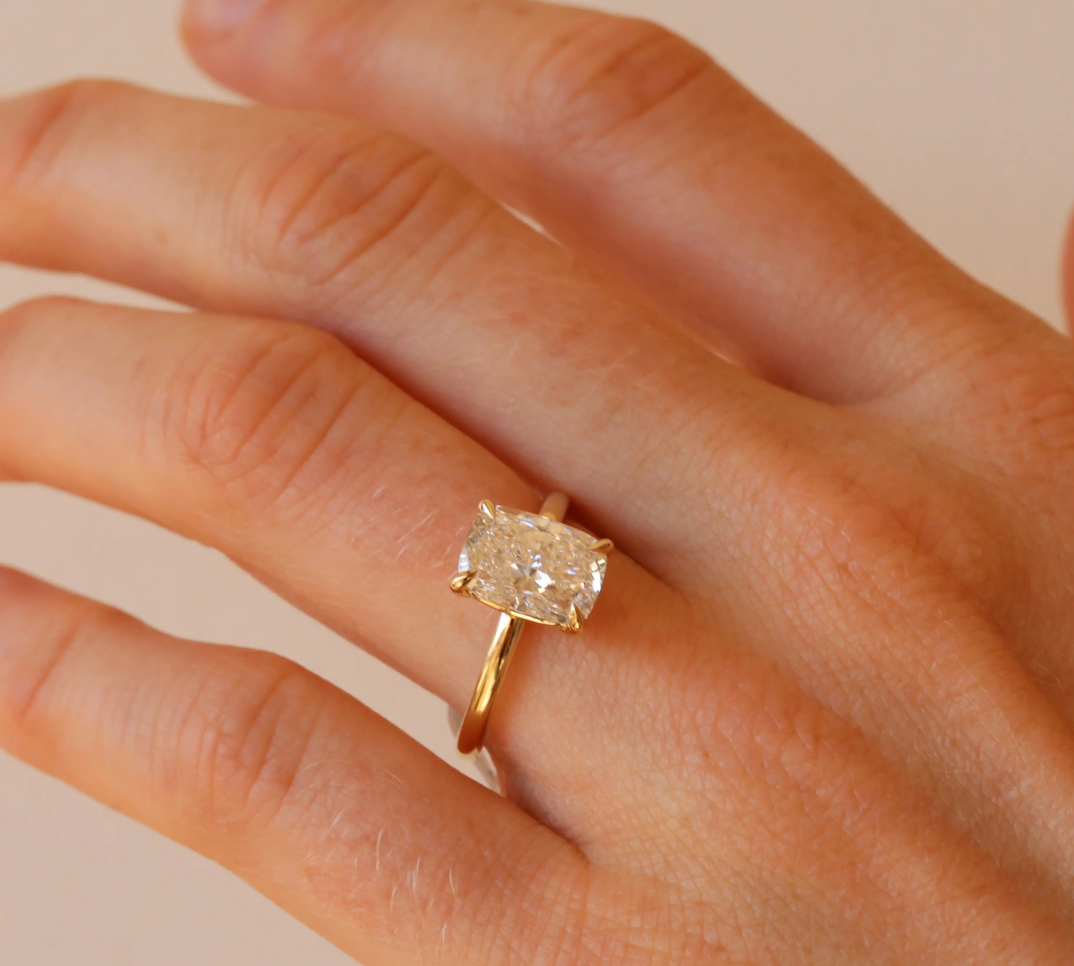 Gold ring with a diamond on a hand against a beige background