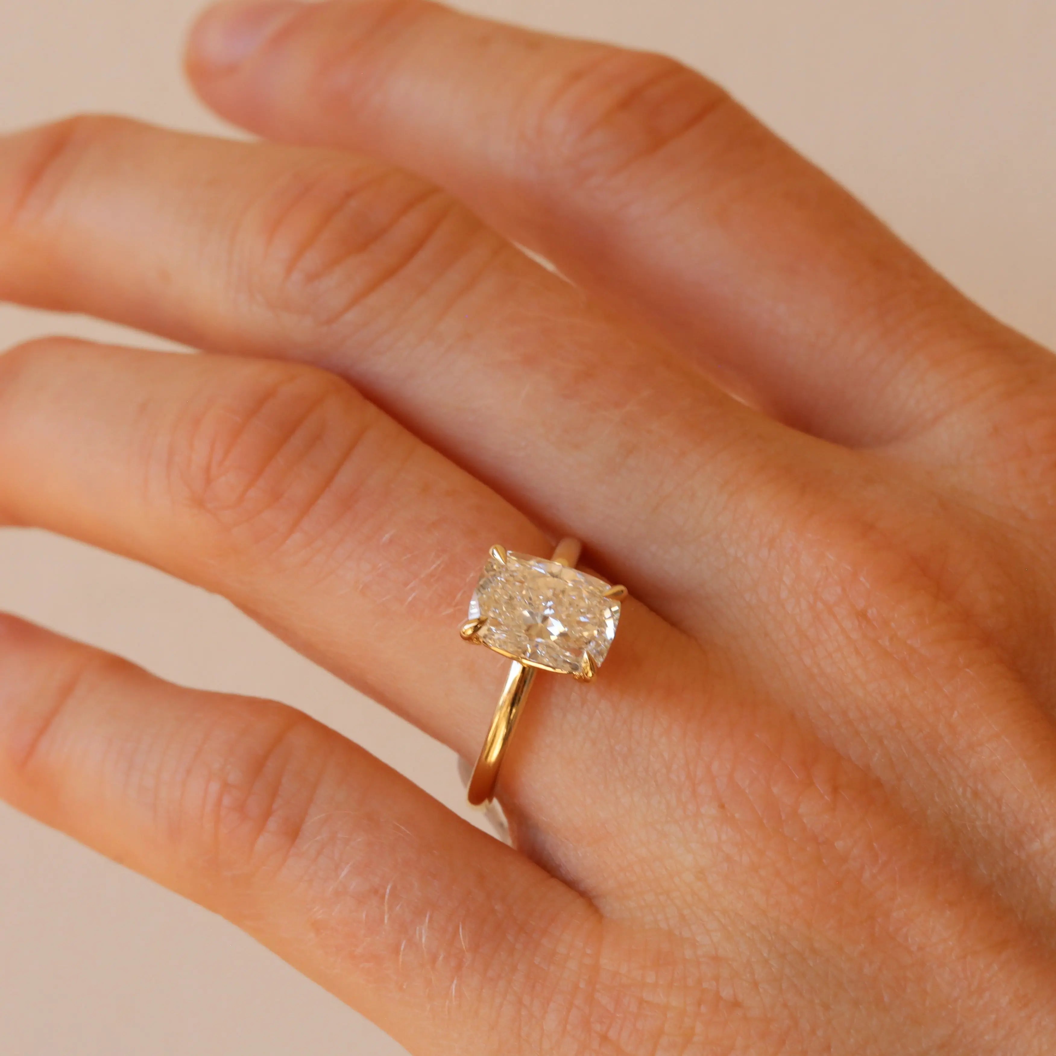 Gold ring with a diamond on a hand against a beige background