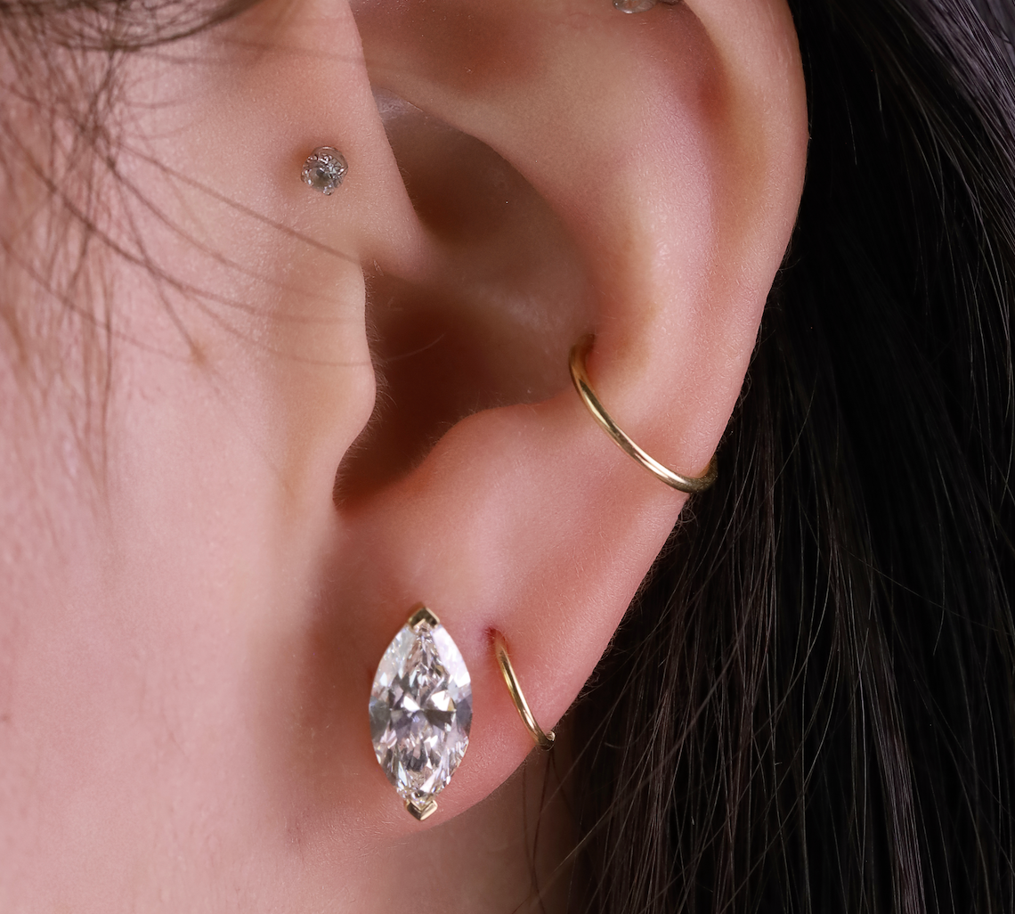 Close-up of an ear with gold hoop earrings and a marquise-shaped earring.