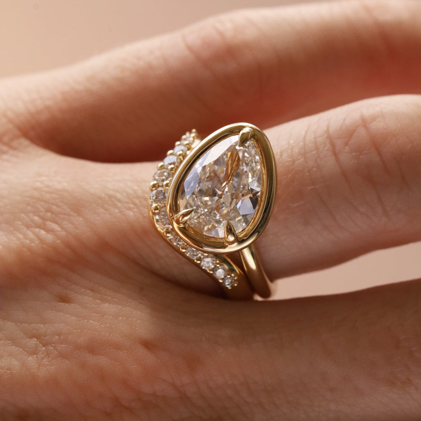 Close up of a tilted pear diamond engagement ring with white diamond stacking band, on hand.