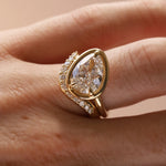 Close up of a tilted pear diamond engagement ring with white diamond stacking band, on hand.
