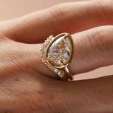 Close up of a tilted pear diamond engagement ring with white diamond stacking band, on hand.