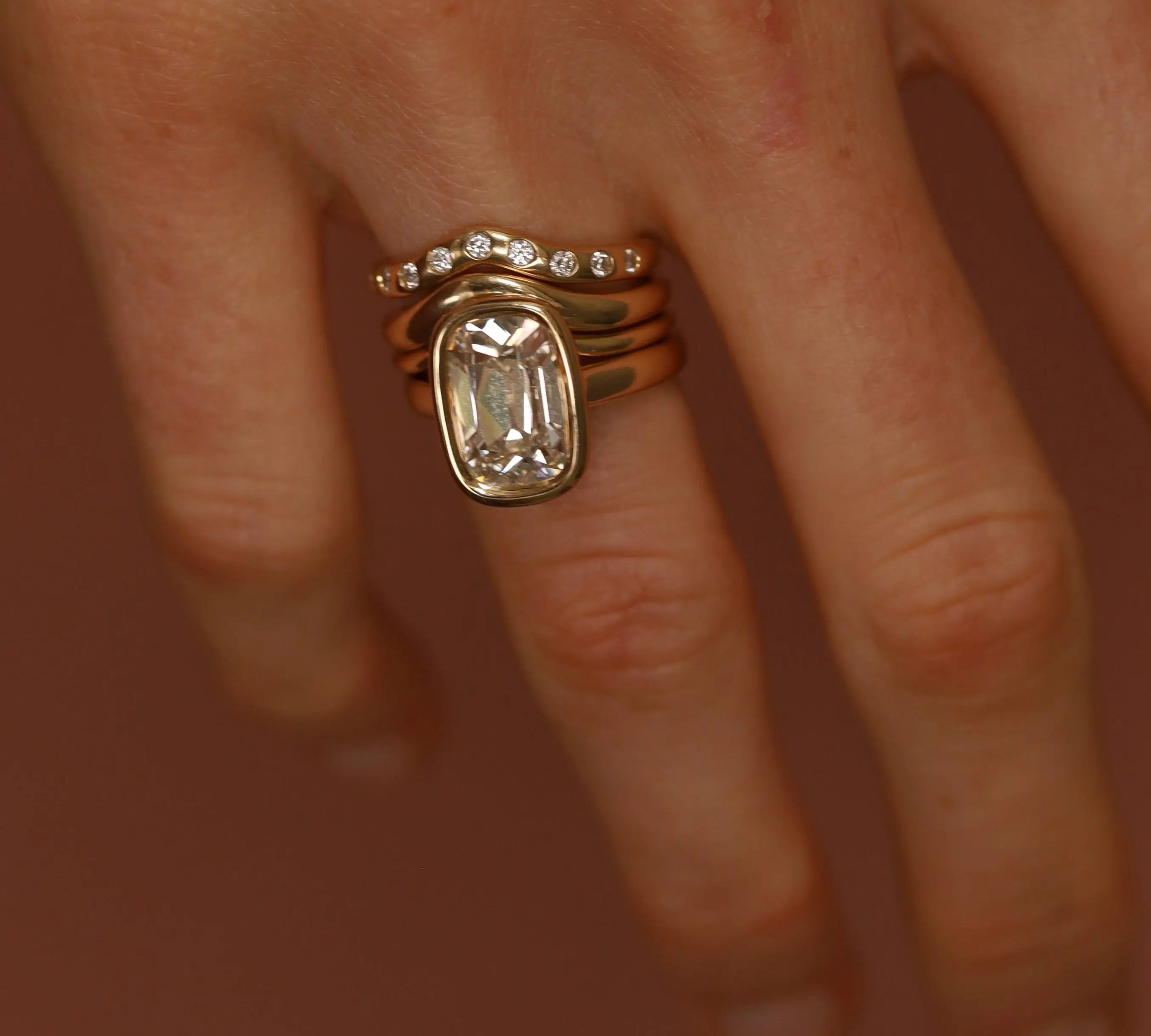 Close-up of a hand wearing two gold rings with gemstones on a blurred background