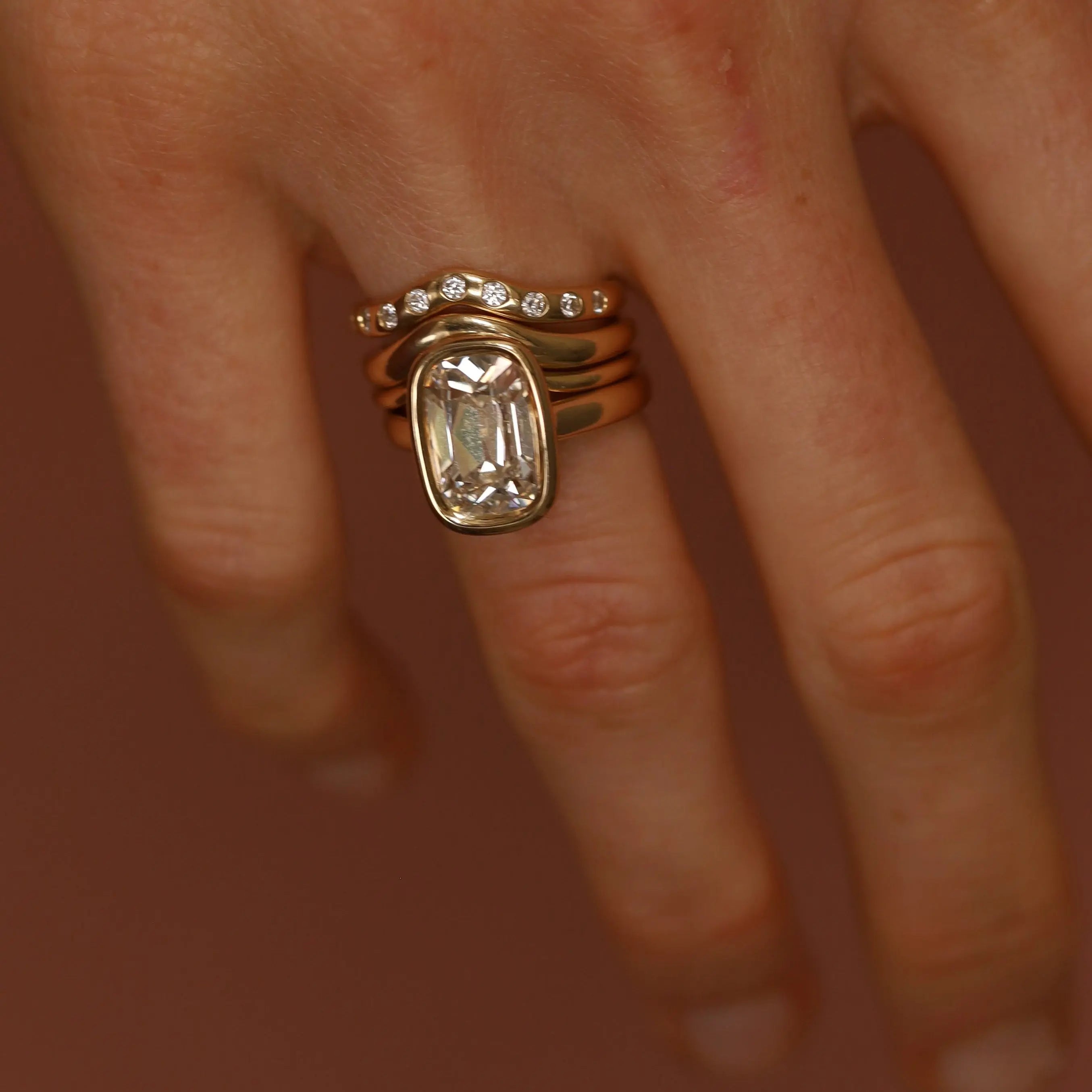 Close-up of a hand wearing two gold rings with gemstones on a blurred background