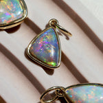 Opal pendant with gold setting on a light pink surface