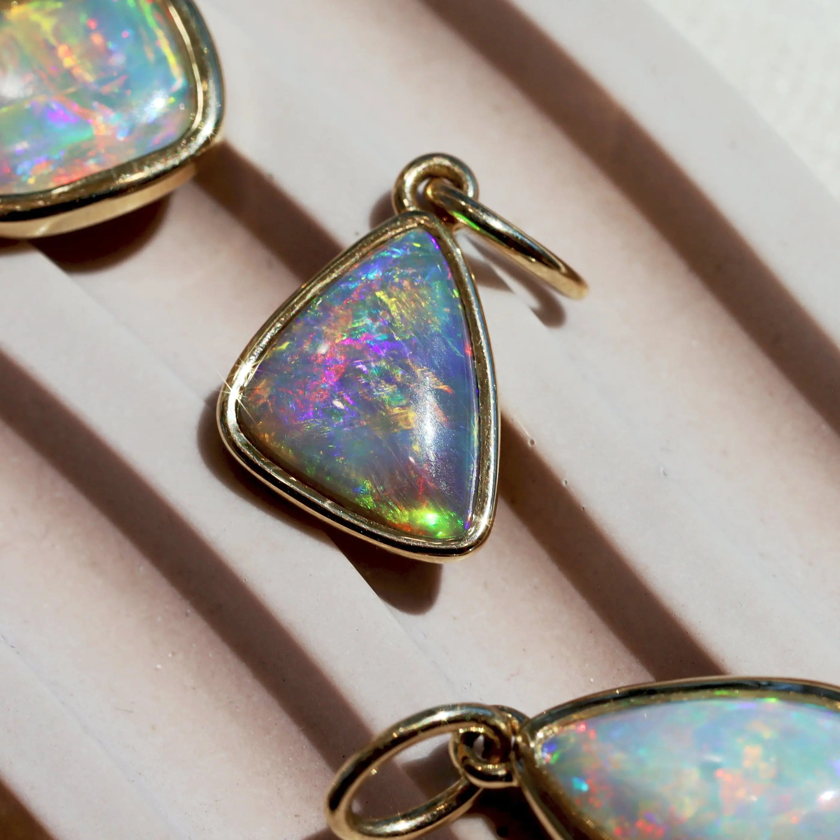 Opal pendant with gold setting on a light pink surface