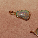 Opal pendant with gold setting on a textured pink surface