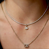 Close-up of model's neck with two necklaces. One tennis necklace with a diamond charm on it, and one gold chain with two rondelle charms