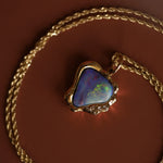 Opal pendant on a gold chain against a brown background