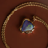 Opal pendant on a gold chain against a brown background