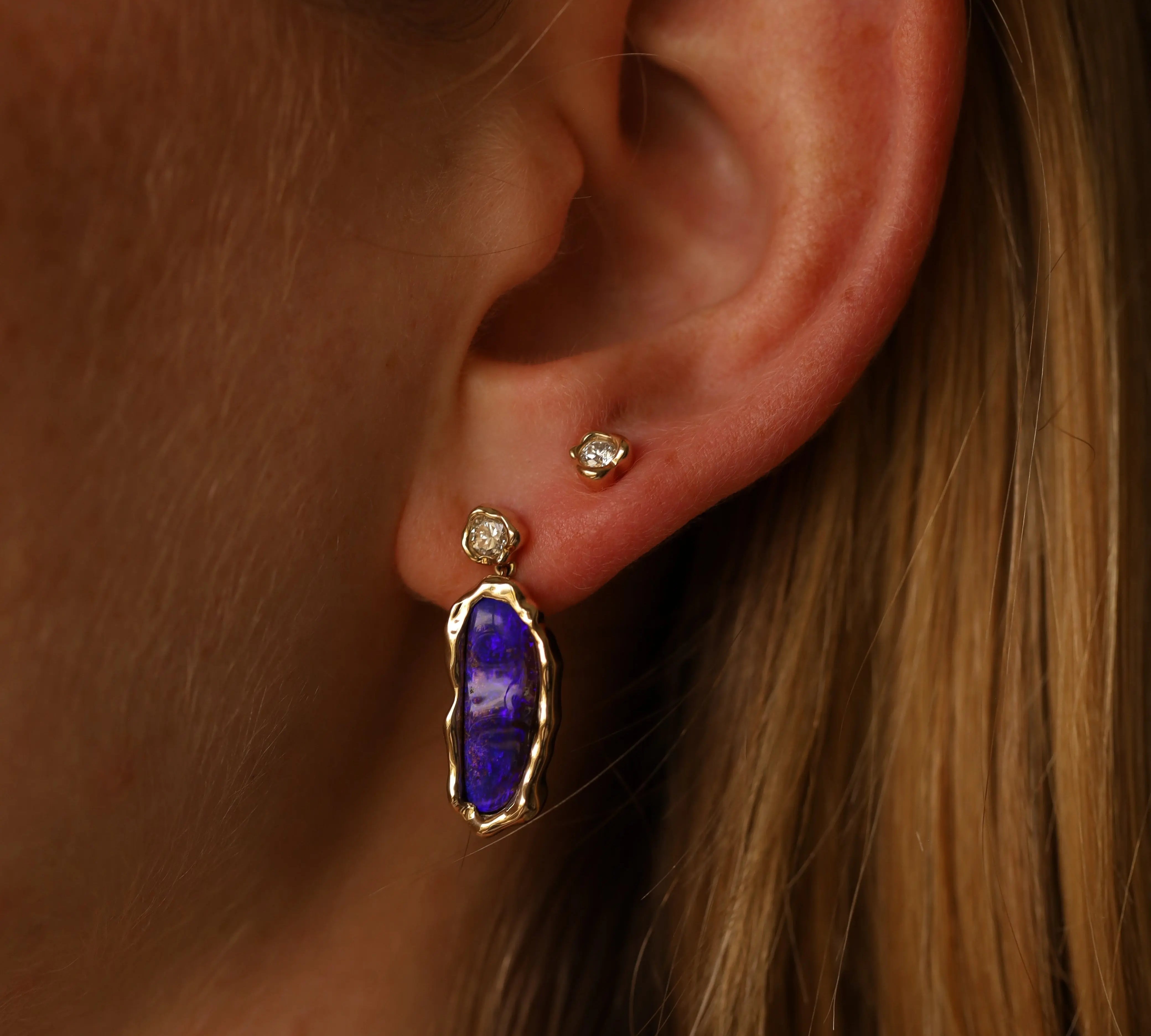 Close-up of an ear with a purple gemstone earring and gold stud.