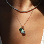 Necklace with a pendant featuring two green gemstones on a person's neck.