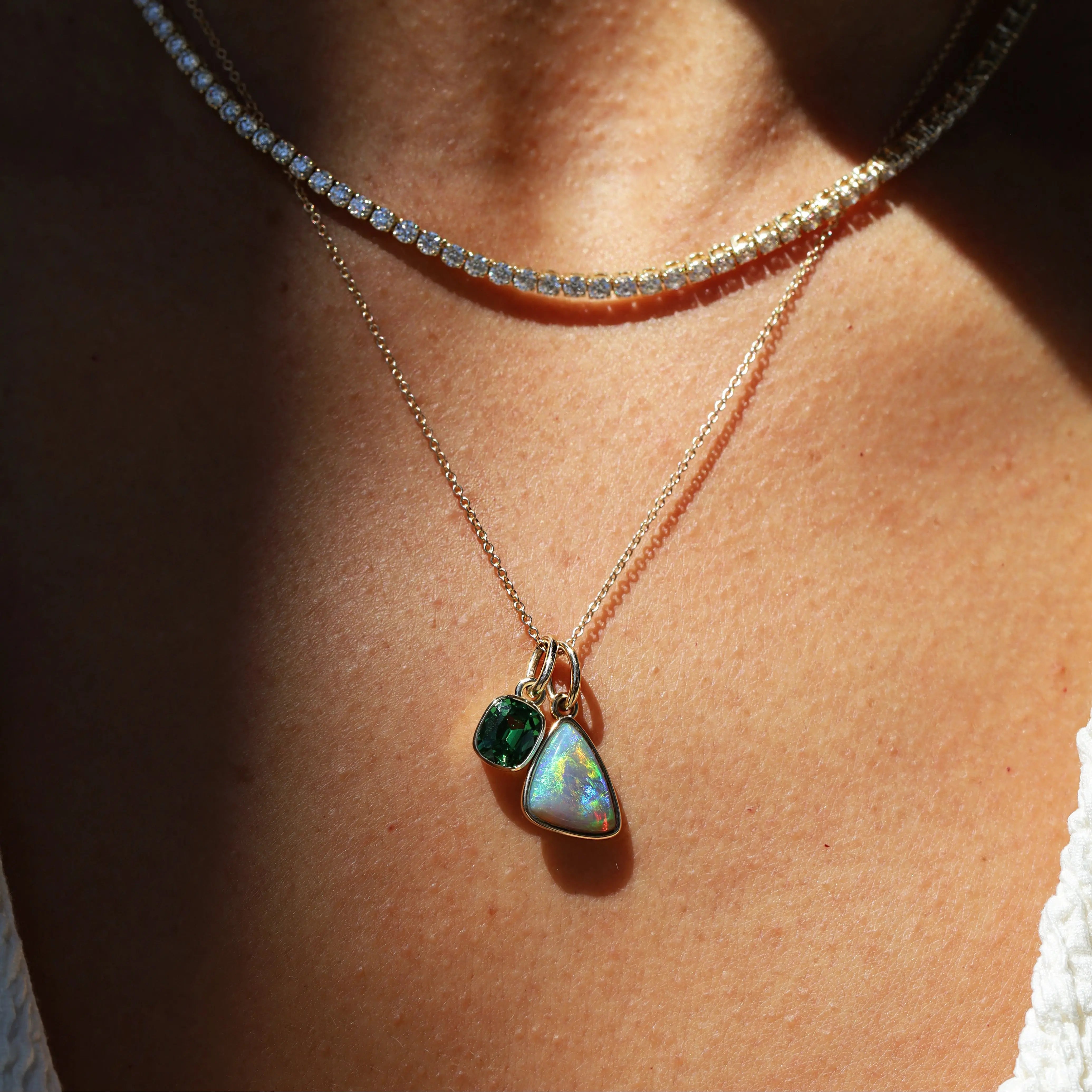 Necklace with a pendant featuring two green gemstones on a person's neck.