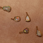 Opal pendants with gold settings on a brown fabric background