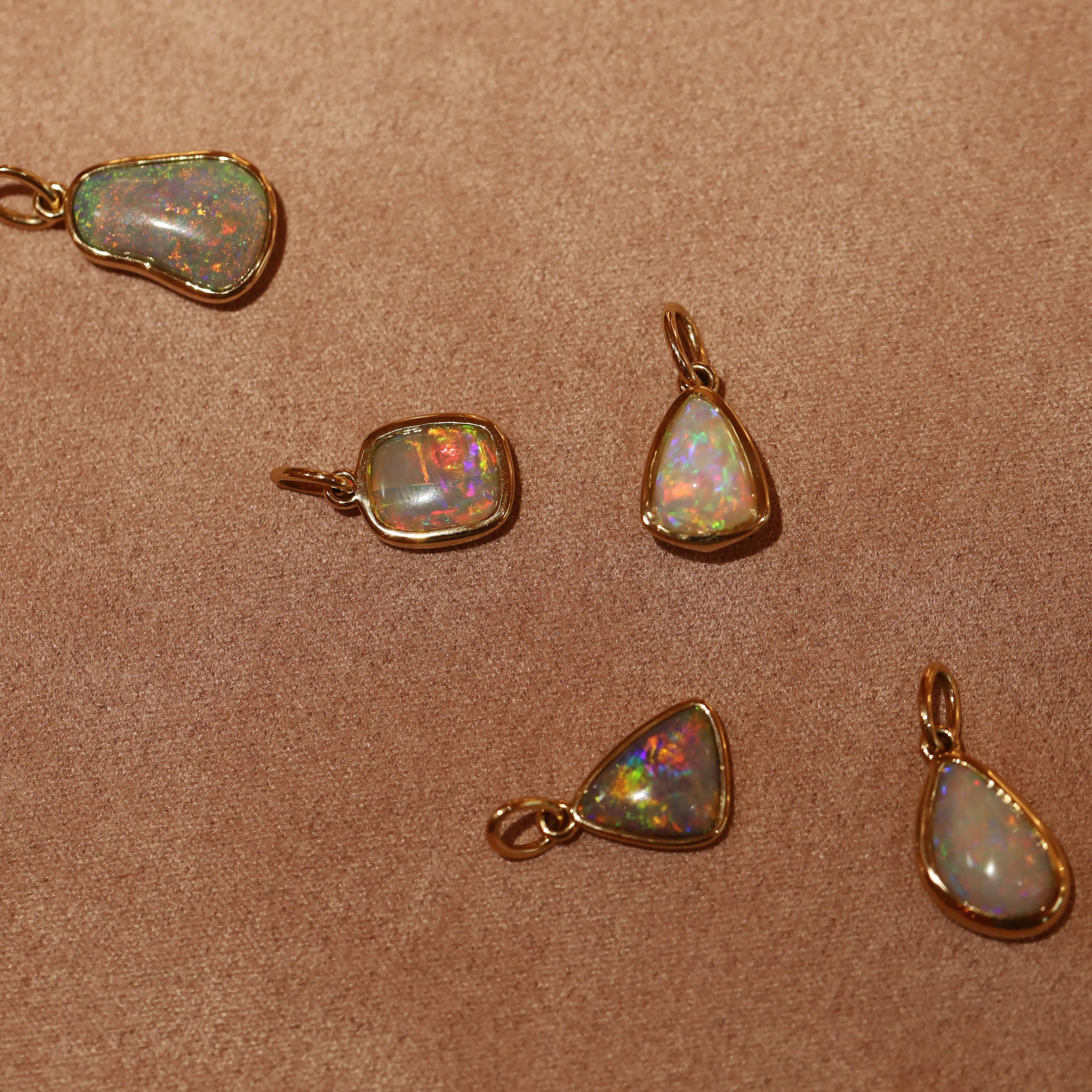 Opal pendants with gold settings on a brown fabric background