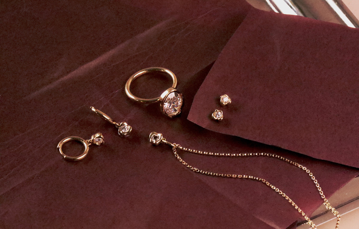 Gold abstract bezel ring, drop earrings, studs and a fine chain laid out on deep burgundy paper