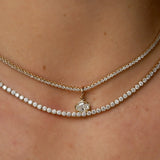 Close-up of model's neck with two tennis necklaces. The thinner necklace has a diamond charm on it.
