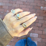 Hand wearing multiple rings with a brick pavement background