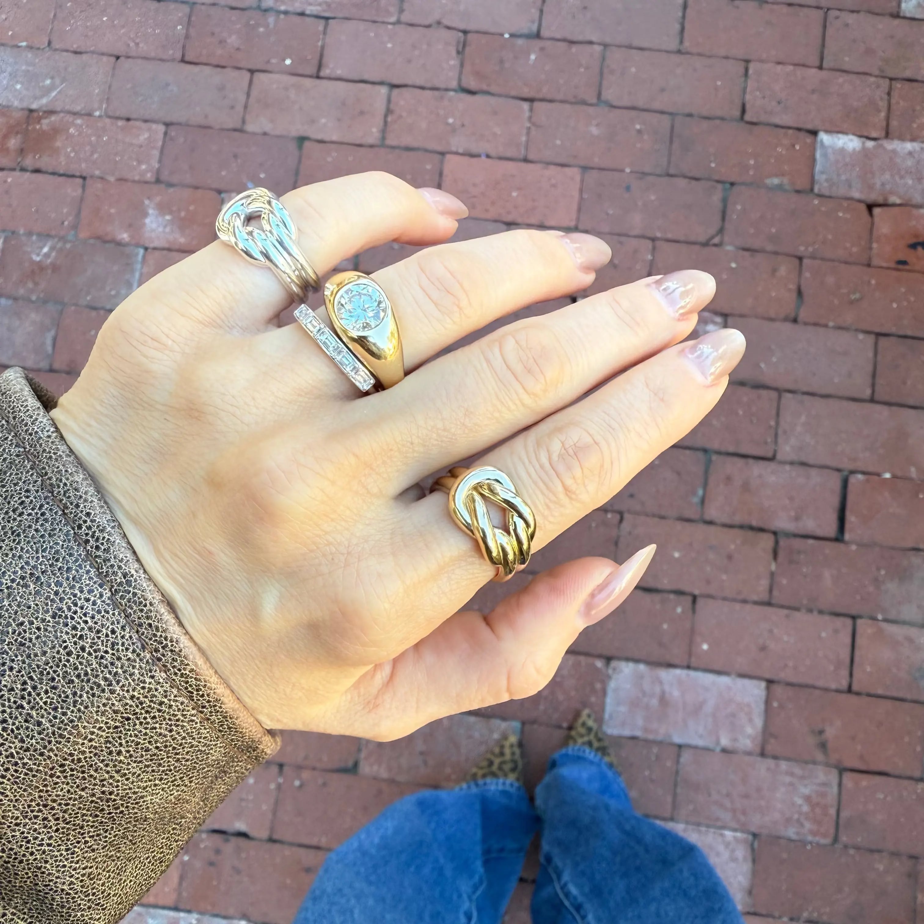 Hand wearing multiple rings with a brick pavement background