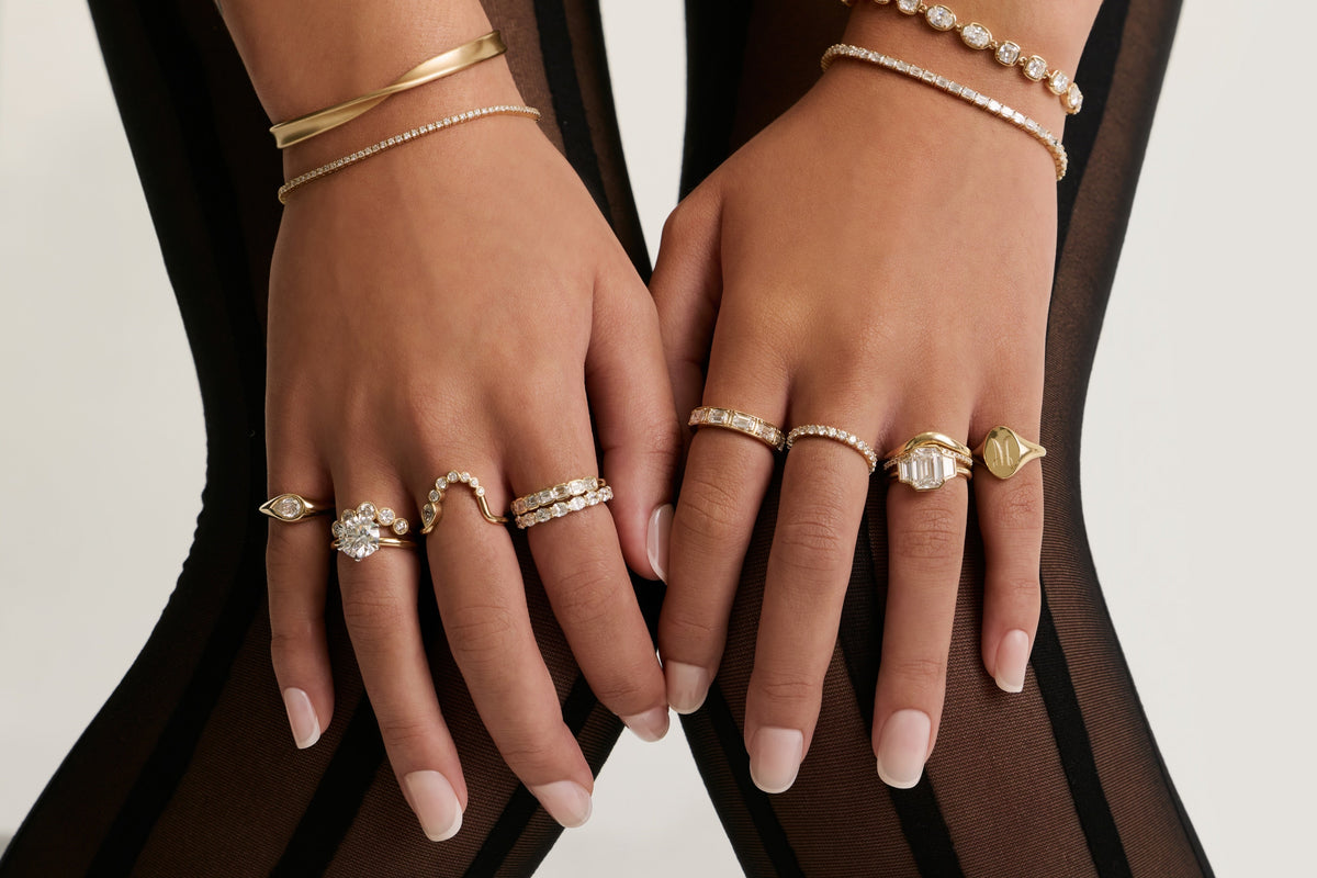 Hands in sheer black sleeves wearing stacked gold bracelets and diamond rings