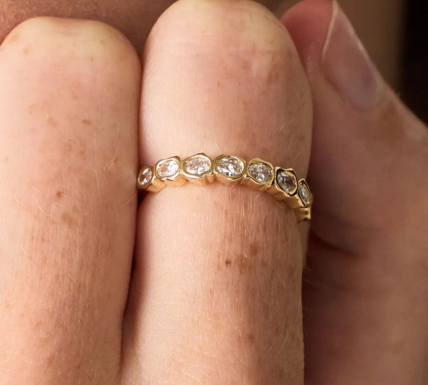 Gold ring with diamonds on a finger against a neutral background