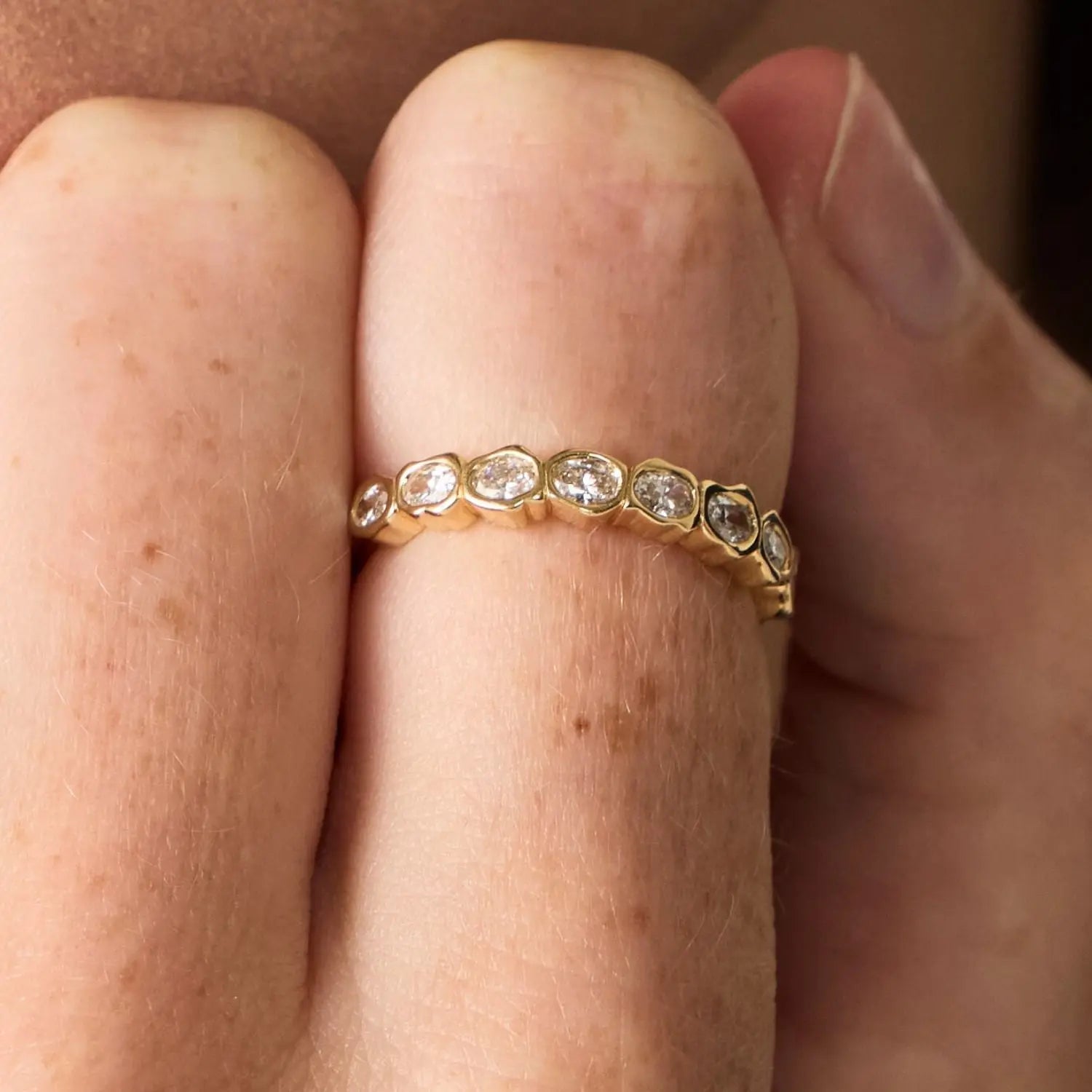 Gold ring with diamonds on a finger against a neutral background