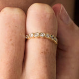 Gold ring with diamonds on a finger against a neutral background