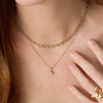 Gold necklace with a small pendant worn by a person, with a hand touching the chest.