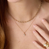Gold necklace with a small pendant worn by a person, with a hand touching the chest.