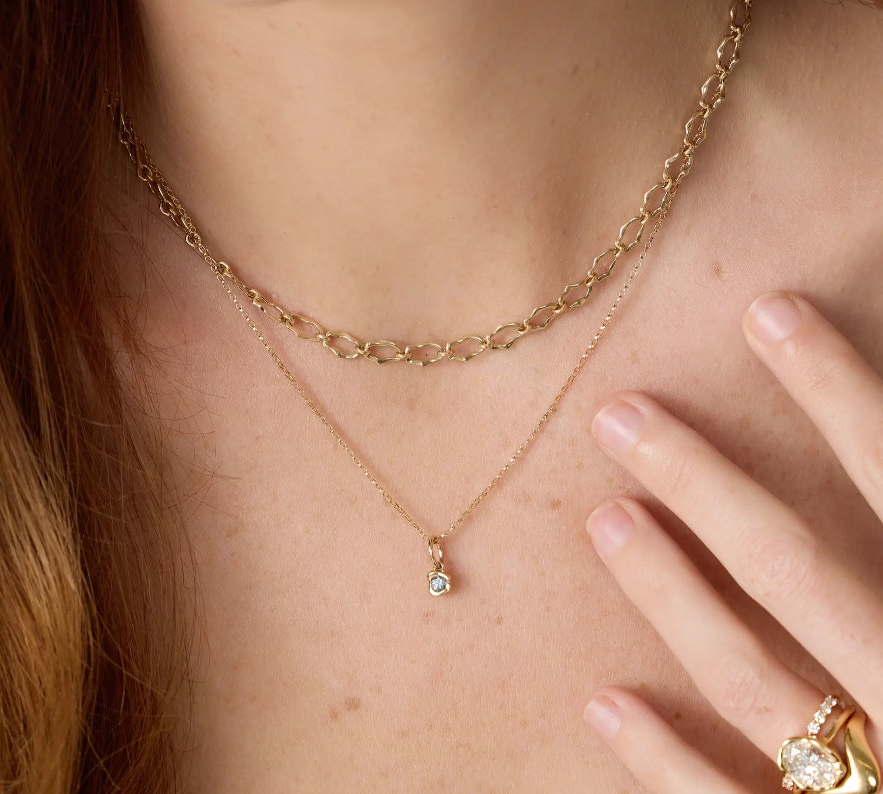 Gold necklace with a small pendant worn by a person, with a hand touching the chest.