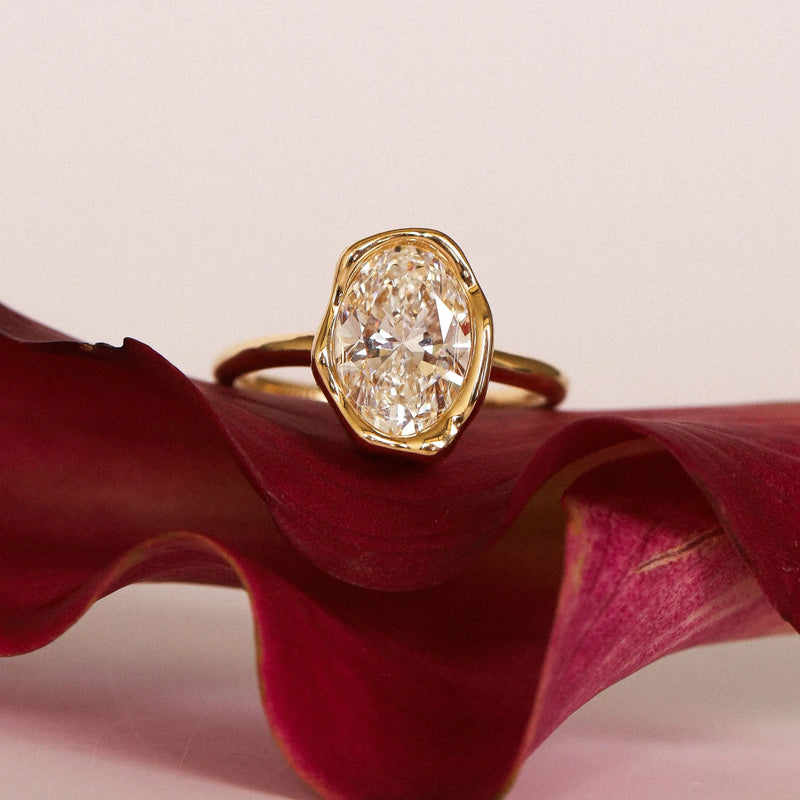 The Abstract Bezel Oval Engagement Ring on a red flower petal